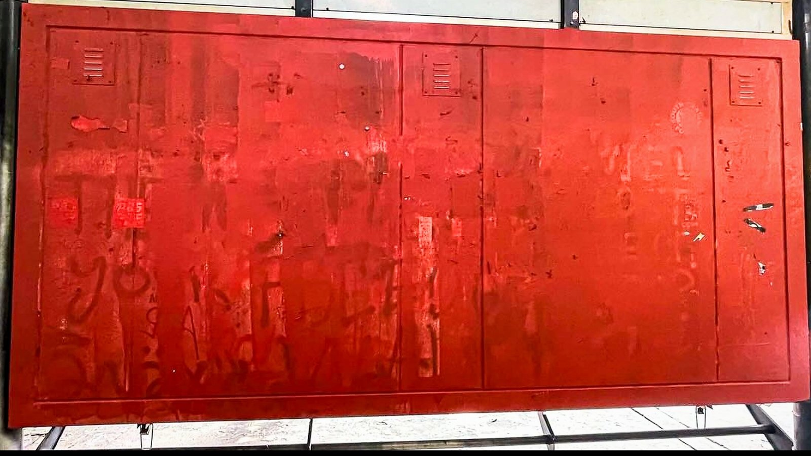 Red panels on an España waiting shed with faint handwritten markings.